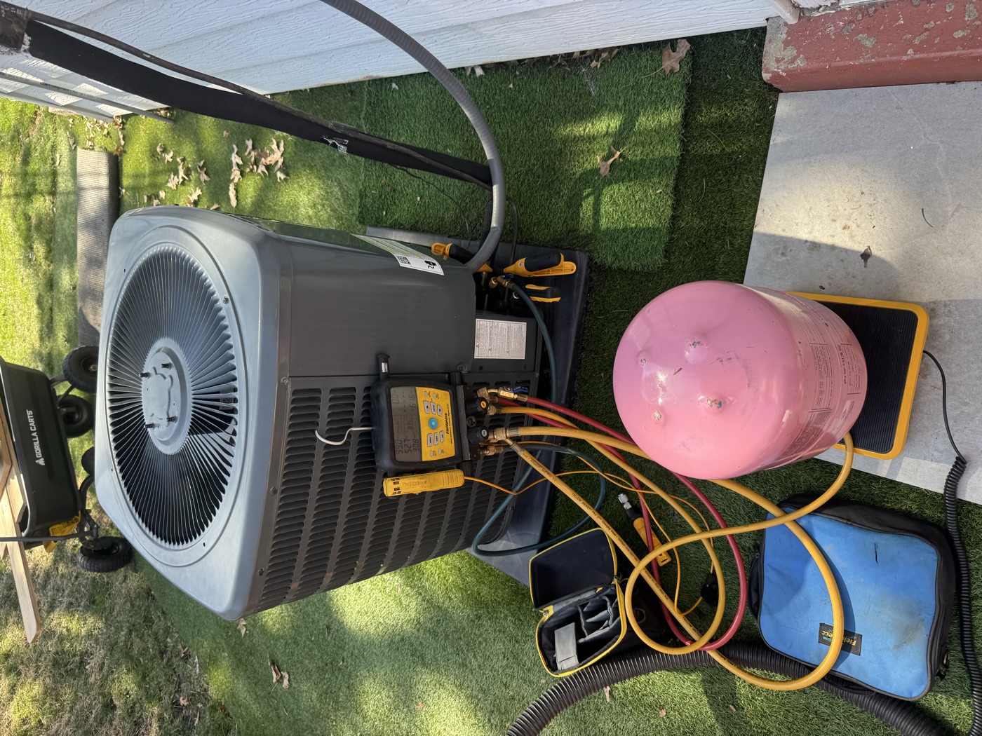 AC unit being serviced with manifold gauges and refrigerant tank